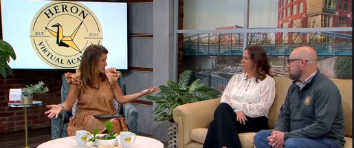 An interviewer sitting on a chair and interviewing two people who are sitting on a couch.